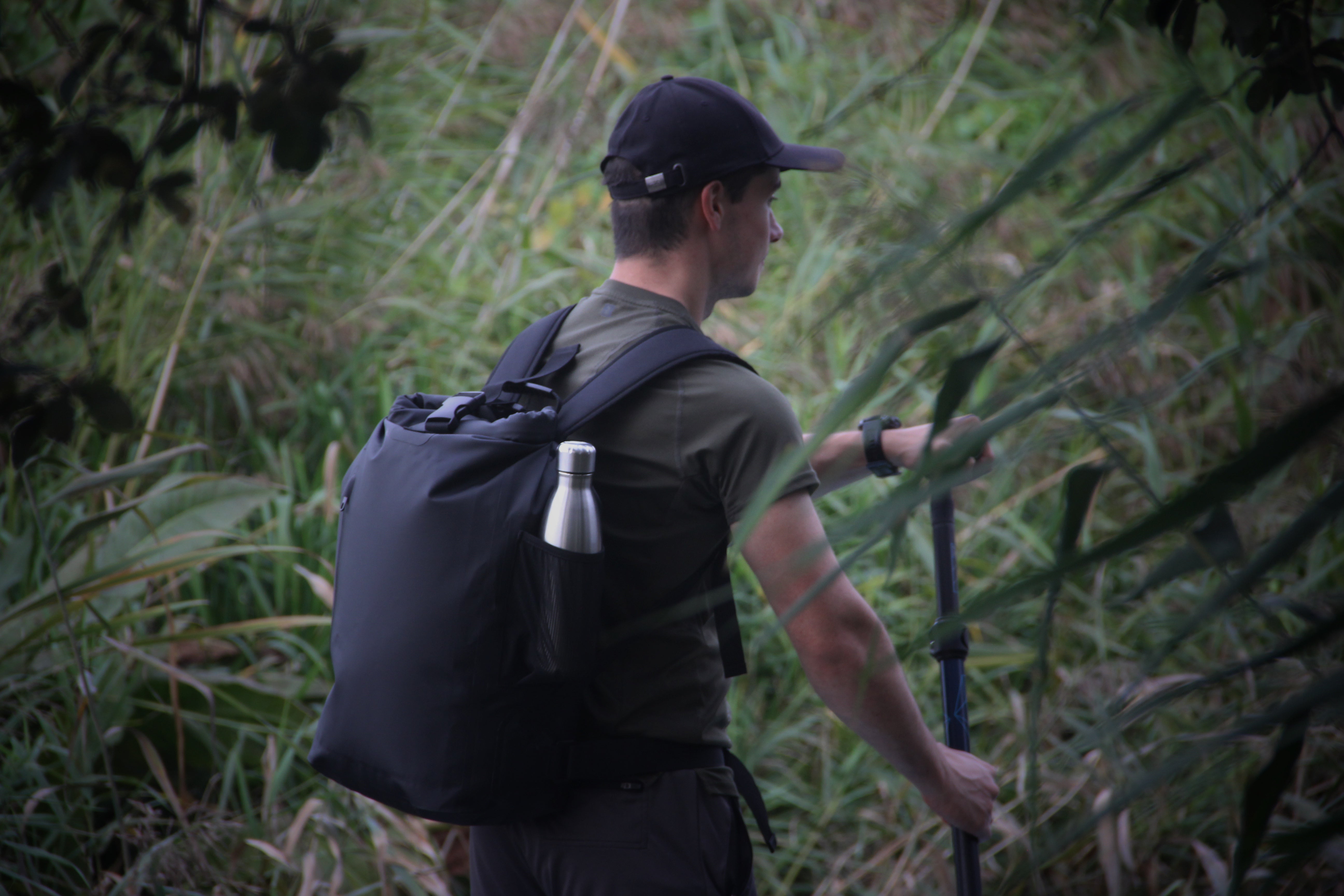 Image of a person paddle boarding on a canal with the Roll Top 30 backpack on their back. 