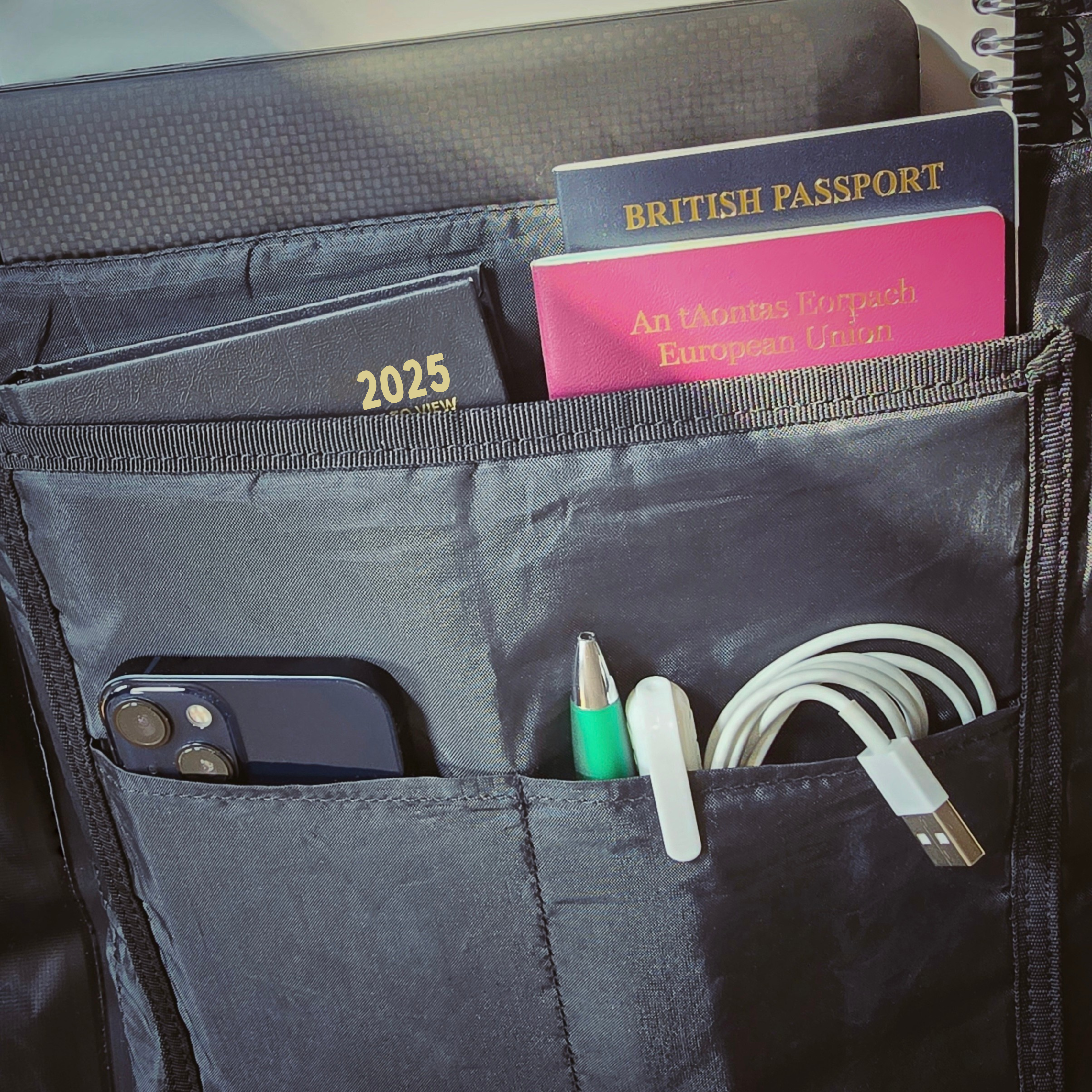 The inside of the Roll Top 30 waterproof backpack. This image shows multiple internal pockets. It highlights the organisational aspect of the backpack. There is  a phone, cables pens, passports, notebooks and a laptop. 